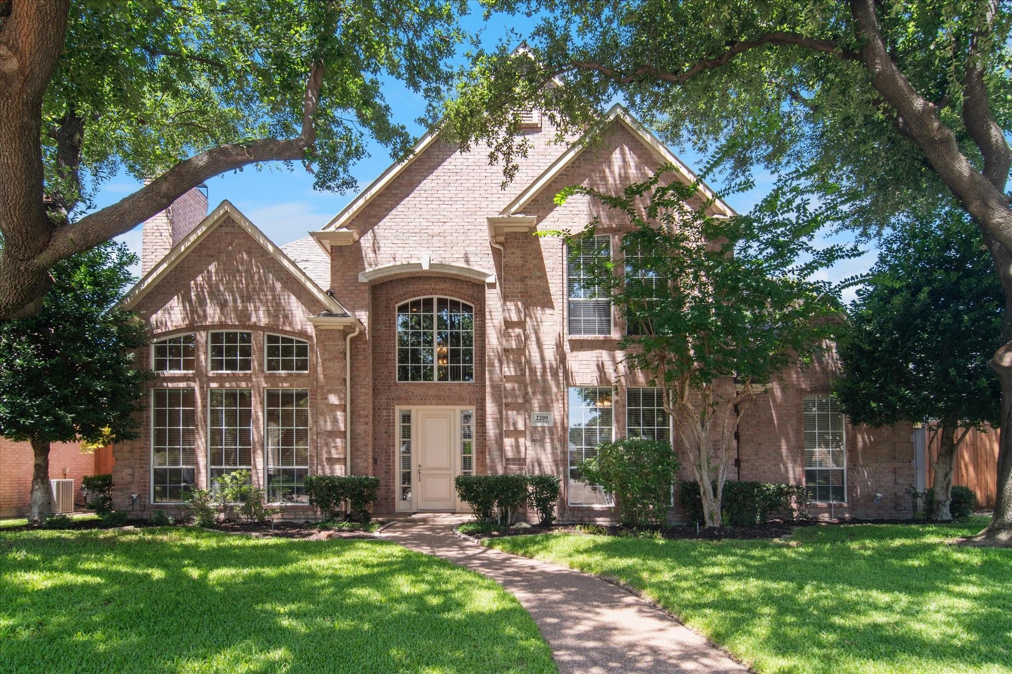 Brick home in Plano with mature trees and a welcoming front entrance